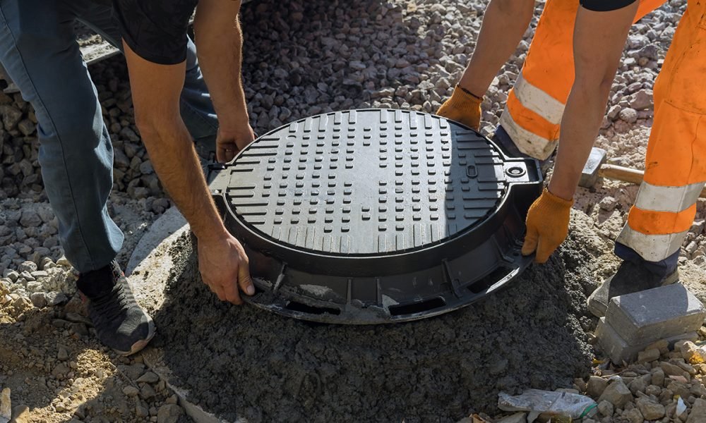 A worker installs a sewer manhole on a septic tank made of concrete rings with construction of sewerage